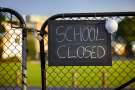 School,closed,sign,with,protective,mask,hanging,on,a,padlocked